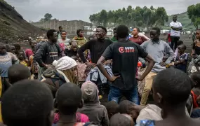 Four young men smile at each other as they lead a group activity. Around them is a large group of people following their lead. 